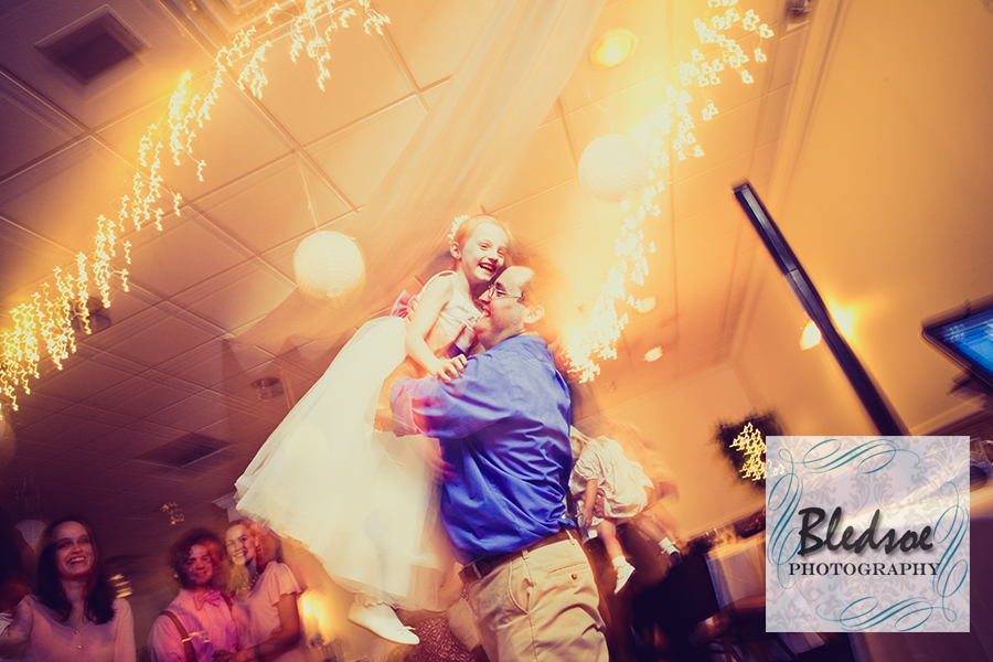 Flower girl lifted in the air by her dad at wedding reception at Rothchild Catering Center.