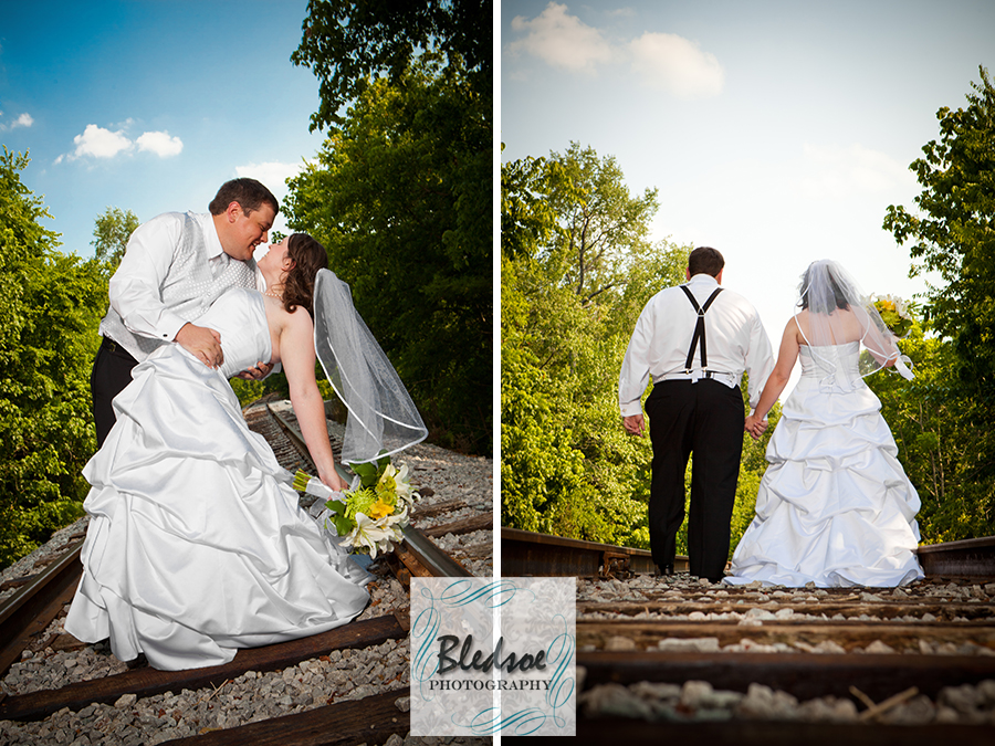 Bride and groom pose on railroad tracks.