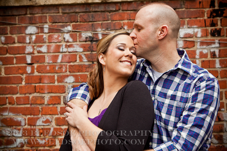 Knoxville engagement photo session in the Old City, couple hugging in front of a red brick wall with graffitti © Bledsoe Photography