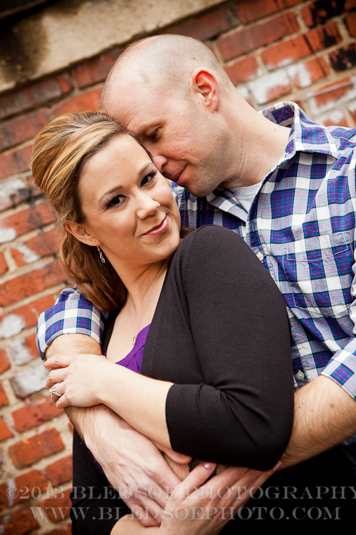 Knoxville engagement photo session in the Old City, couple hugging in front of a red brick wall with graffitti © Bledsoe Photography