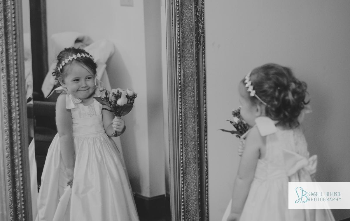 Flower girl grins at herself in the mirror, black and white