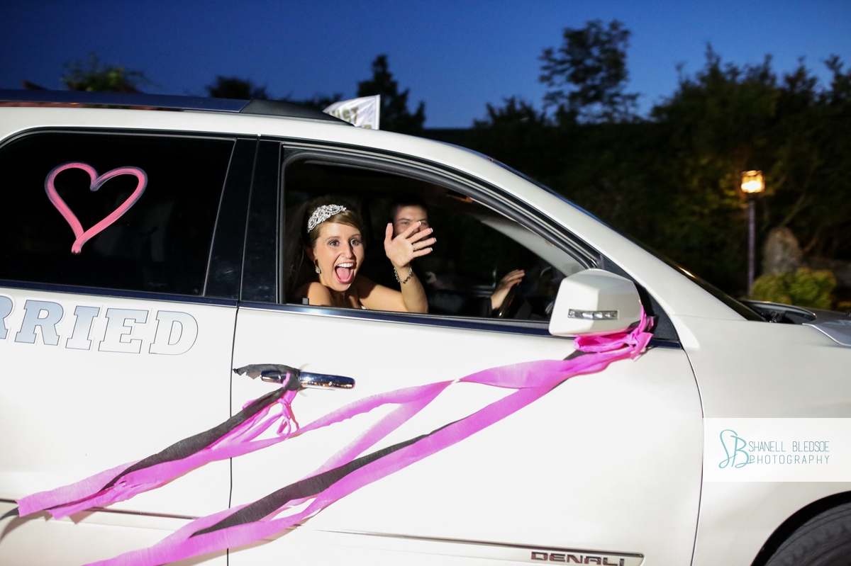 Bride waving goodbye from getaway car after wedding reception