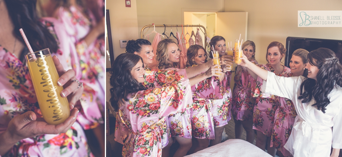 bride and bridesmaids in floral pink robes wedding toasting mimosas on hotel bed