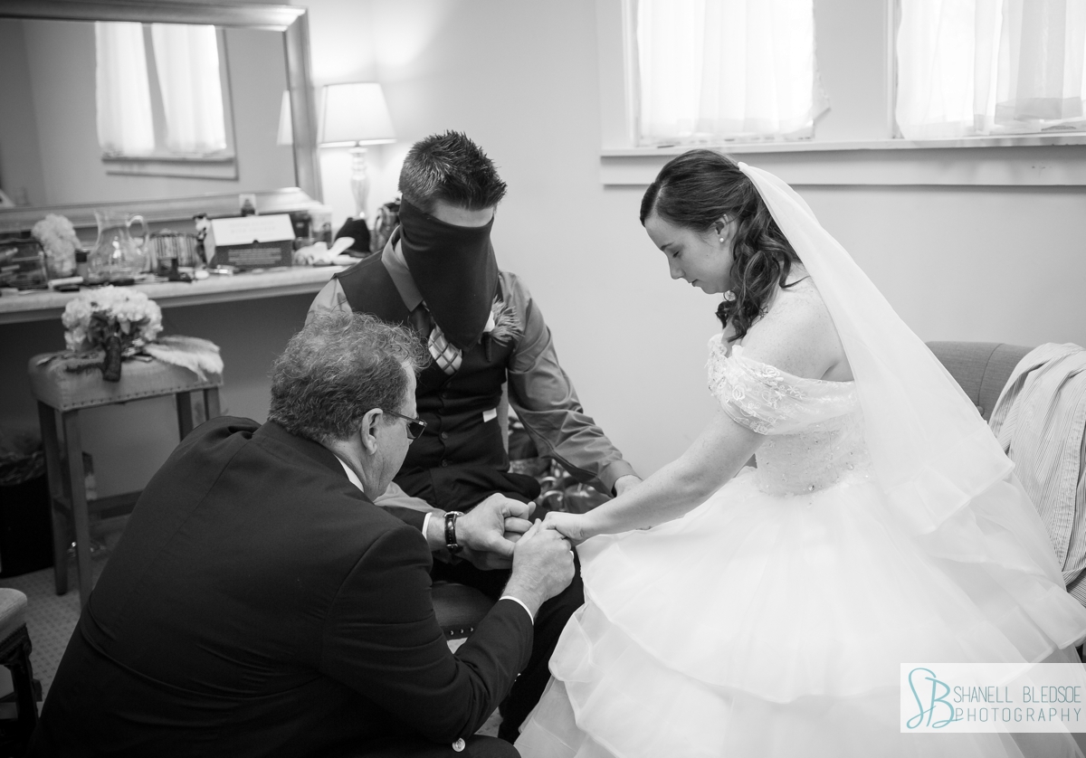 bride and blindfolded groom praying before wedding ceremony