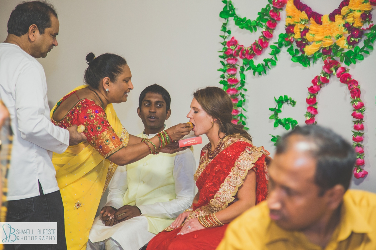 Indian - american bride and groom at haldi pithi ceremony fed by mother