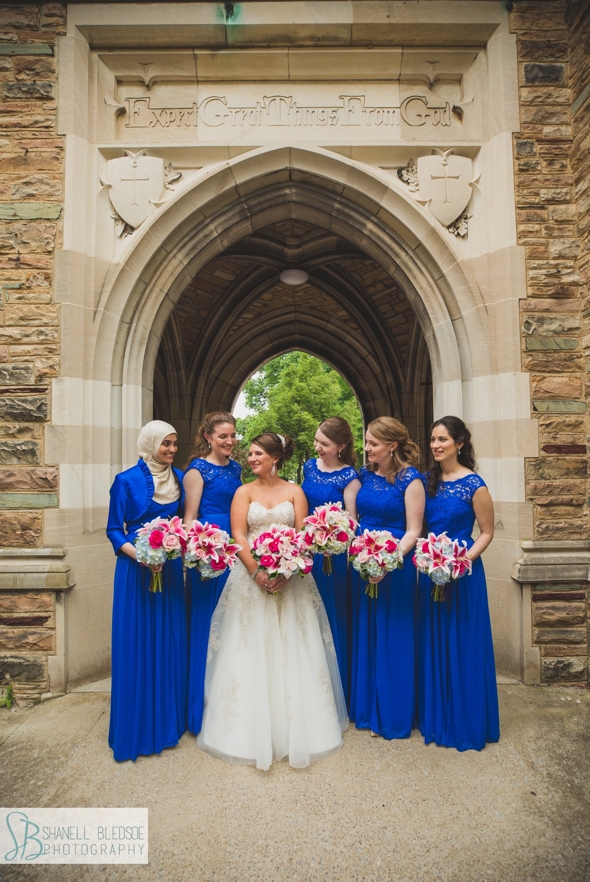 bride with bridesmaids in royal blue lace dresses under arch at Scarritt Bennett Center wedding