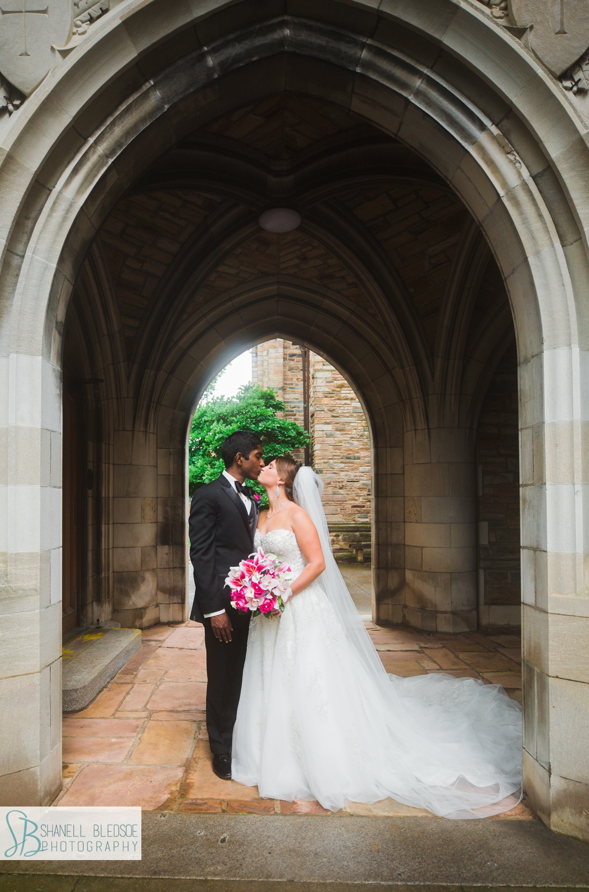 portrait of bride and groom under arch at Scarritt Bennett in Nashville with pink stargazer lily bouquet