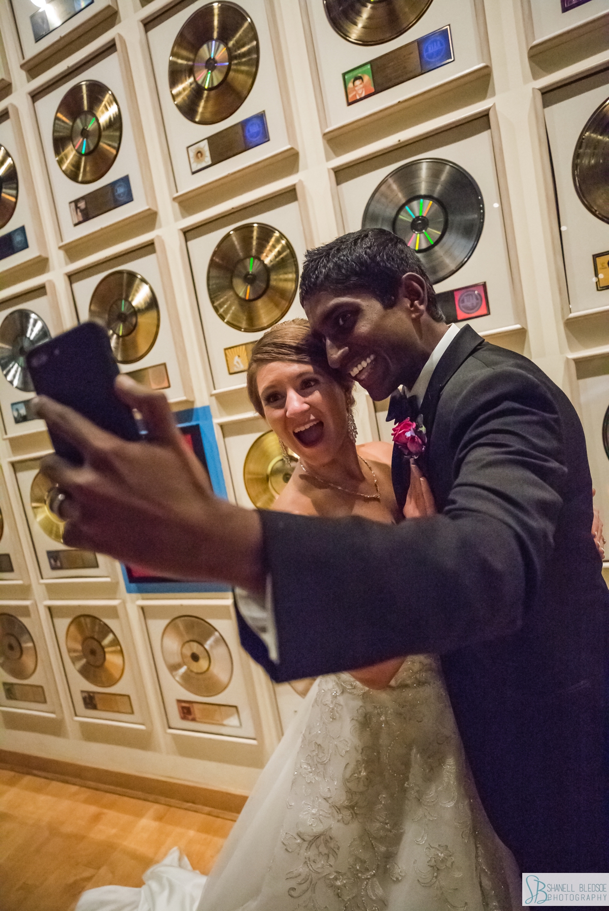 bride and groom selfie in front of the wall of gold records at Country Music Hall of Fame