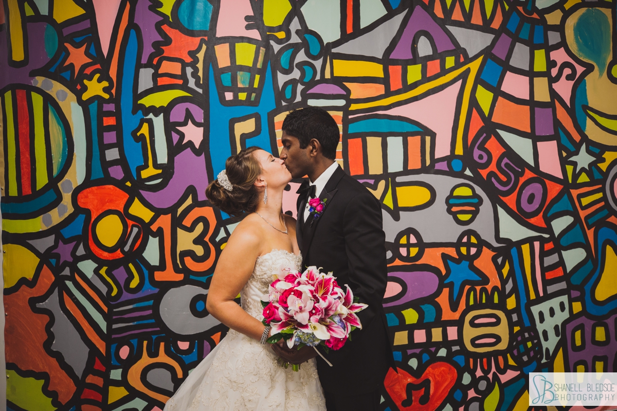 bride and groom kiss in front of colorful mural at Country Music Hall of Fame